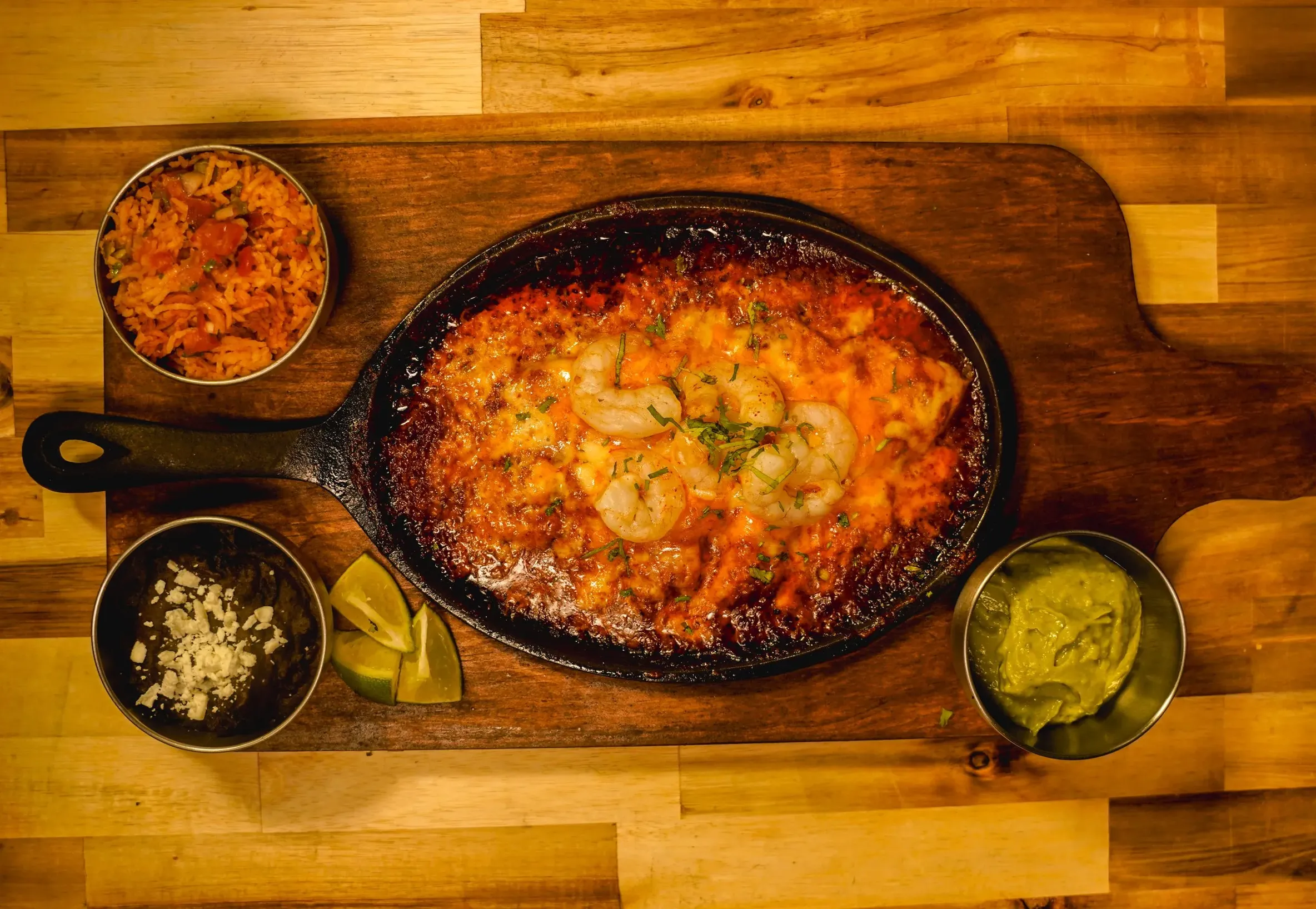 Cast iron skillet of bubbling melted cheese with shrimp, seasoned rice, dips and lime at DJ Donair & Poutine in south Edmonton